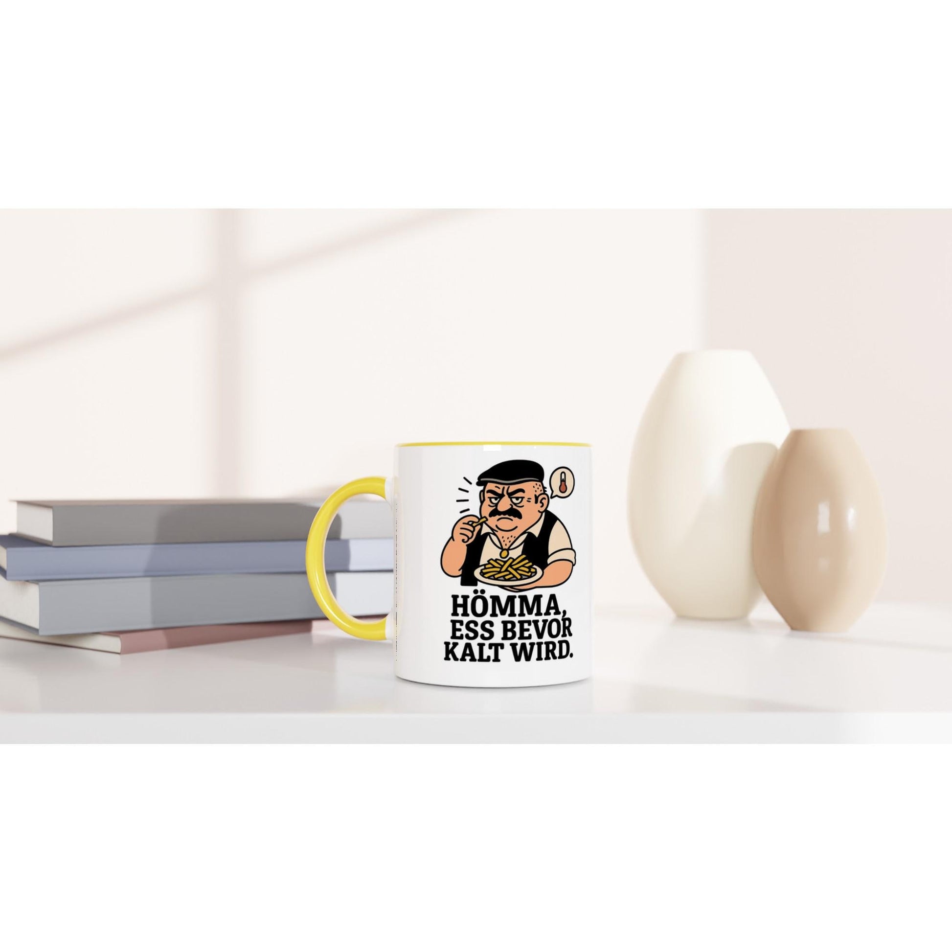 Keramiktasse mit Spruch Geschenk Homma ess bevor kalt wird mit gelbem Henkel auf weißem Tisch