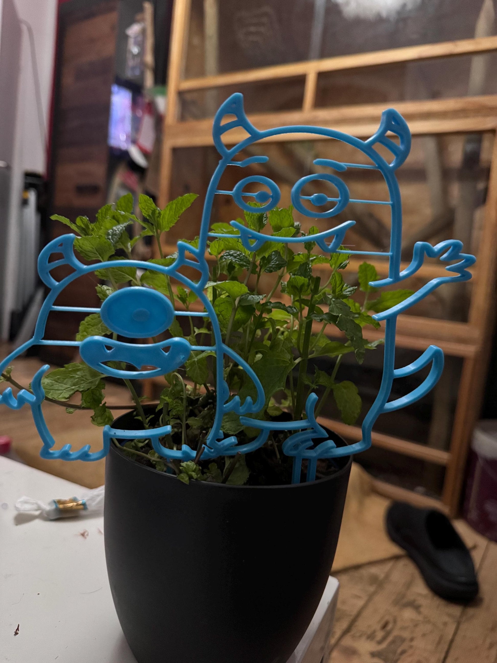 Lustige Deko für Blumentopf in Form von zwei blauen, cartoonartigen Figuren aus Kunststoff im schwarzen Blumentopf