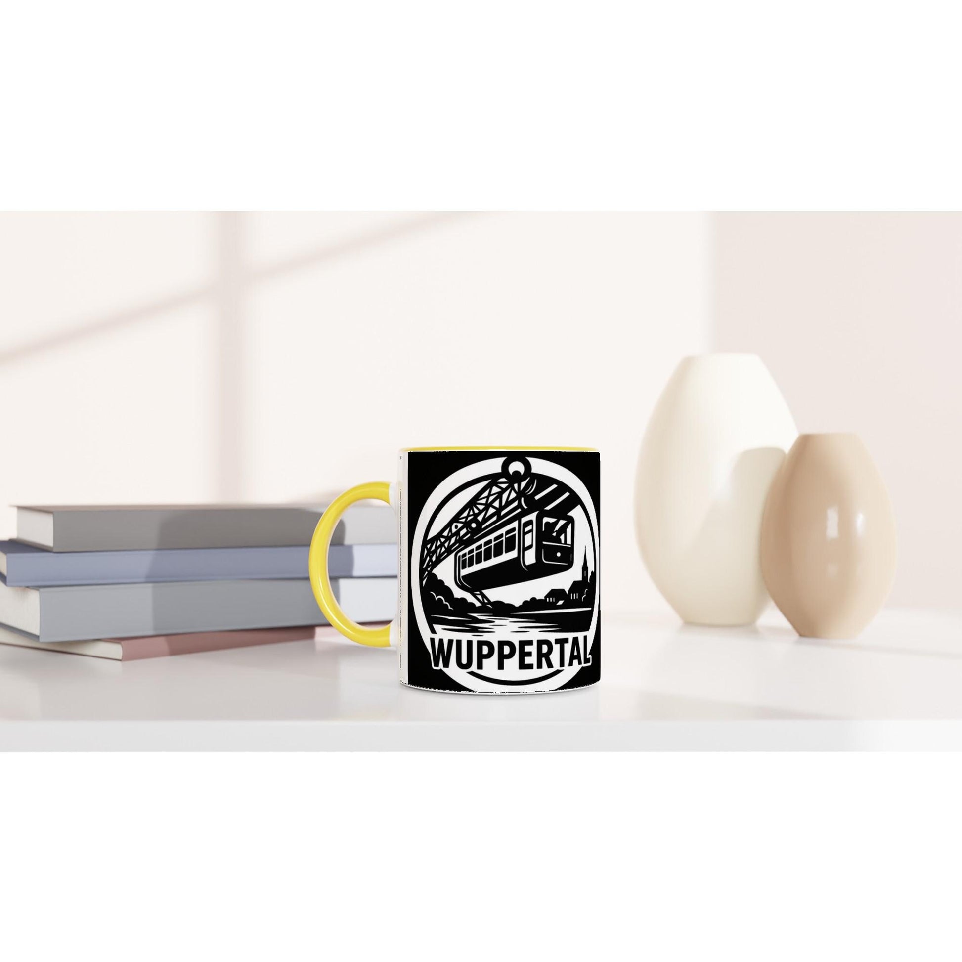 Weiße Wuppertal Schwebebahn Tasse mit schwarzem Motiv und gelbem Henkel auf weißem Tisch